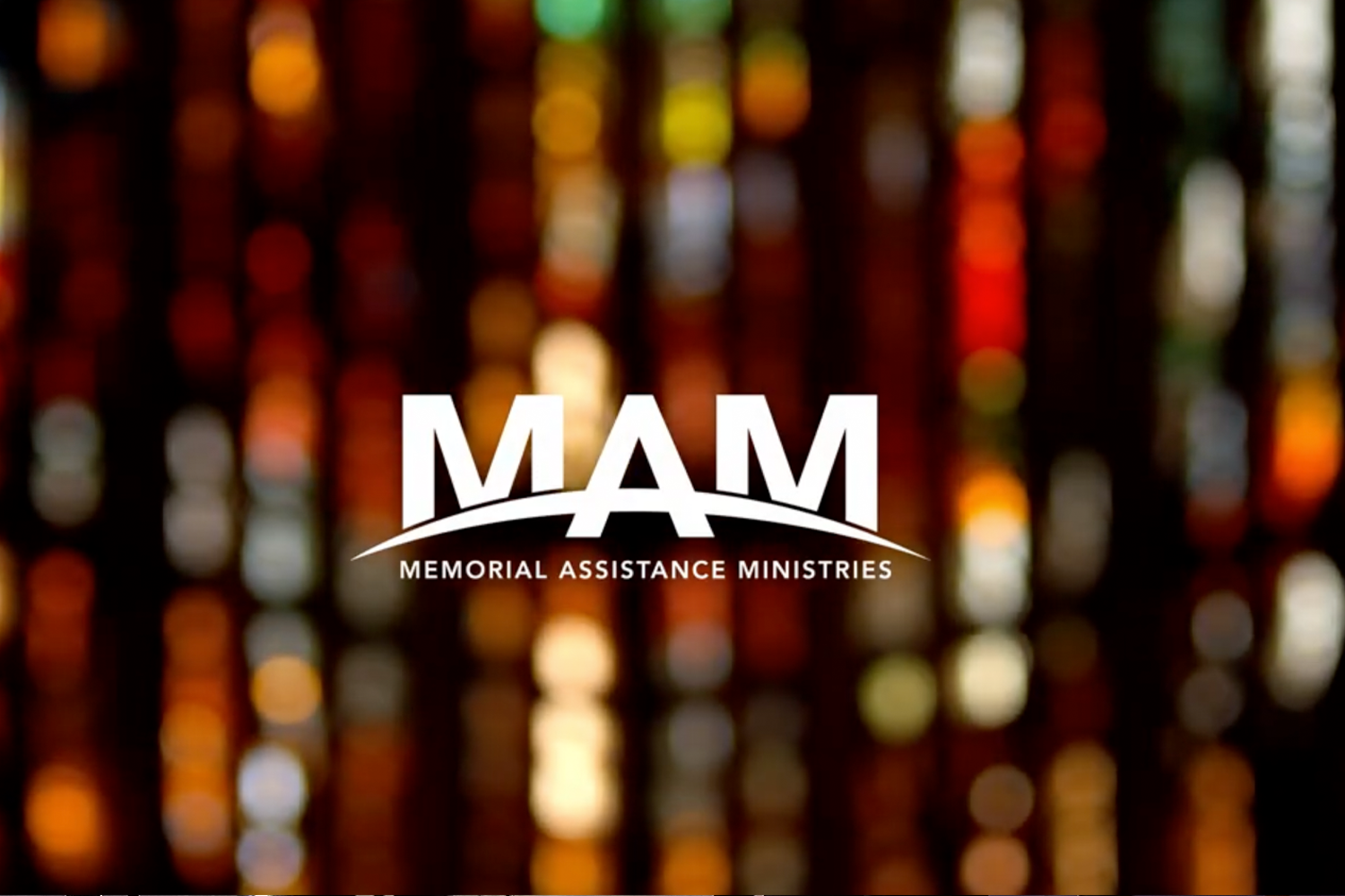 Memorial Assistance Ministries MAM logo against warm event lighting at the annual fundraiser.